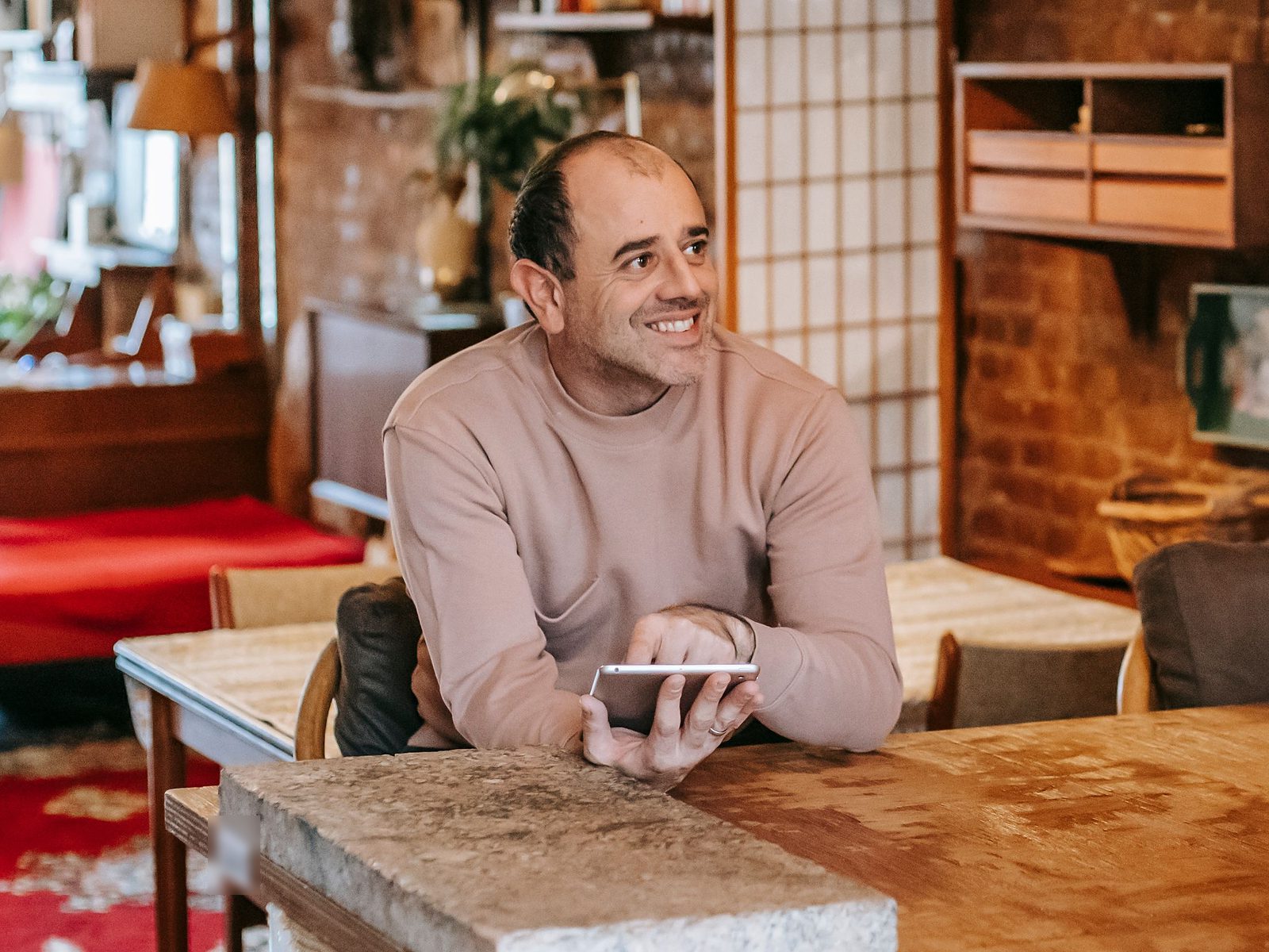 Homem sorrindo com o celular na mão, encostado na mesa da cozinha