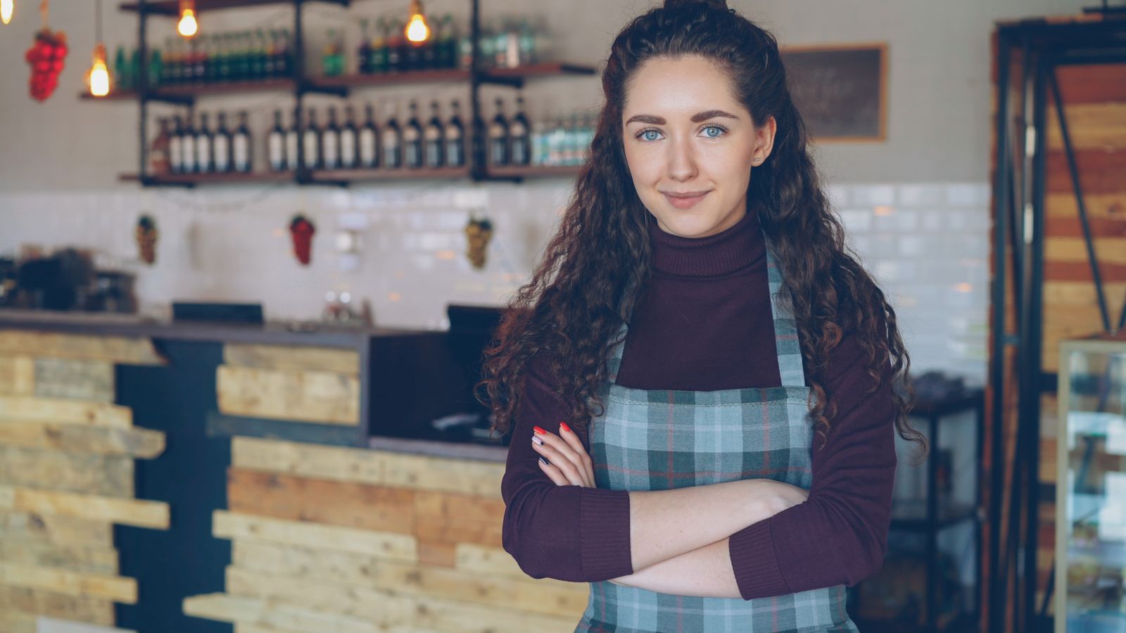Dona de restaurante sorrindo de braços cruzados no salão